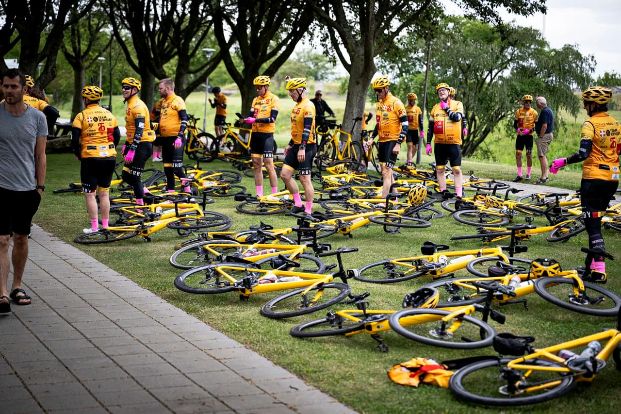 Team Rynkeby-ryttere holder pause ved deres gule cykler i græsset
